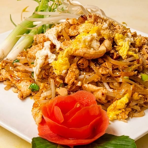 Chicken Pad Thai with noodles, scrambled egg, bean sprouts, green onions, and a tomato rose.