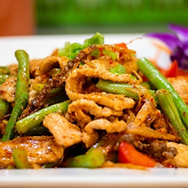 Spicy stir-fried pork with green beans, red bell peppers, and onions, garnished with a purple orchid.