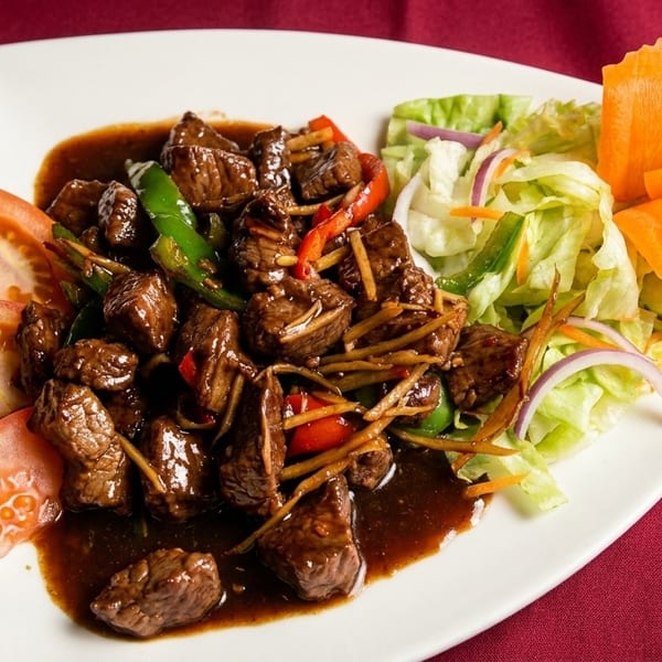 Savory beef stir-fry with bell peppers, ginger, and a side salad with carved carrot garnish.